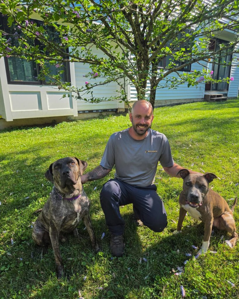 Reliance Contracting & Services team member smiling in a backyard with two dogs